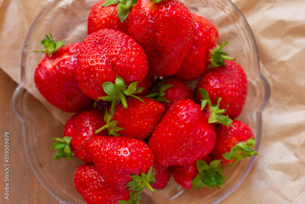 Many red strawberries on glass plate and wooden table top view Many red strawberries on glass plate and wooden table top view