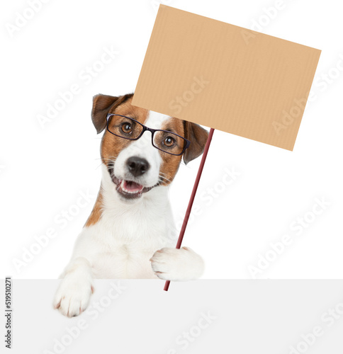 Smart puppy looks above empty white banner and holds blank banner mock up on wood stick. isolated on white background © Ermolaev Alexandr