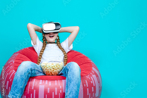 Virtual Technology Ideas. Winsome Teenage Female in White Shirt Posing in Modern Virtual Reality VR Helmet With Popcorn And Excited Expression photo