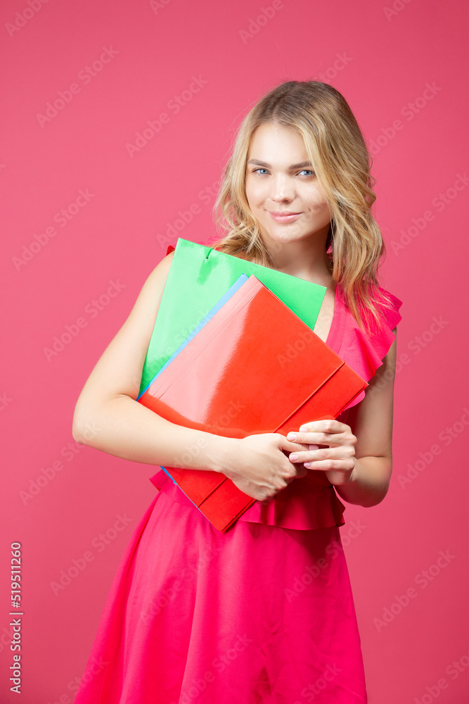 Young Winsome Smiling Caucasian Girl in Red Summer Dress With Colorful Folders Against Coral Background. Young Winsome Smiling Caucasian Girl in Red Summer Dress With Colorful Folders Against Coral Background.