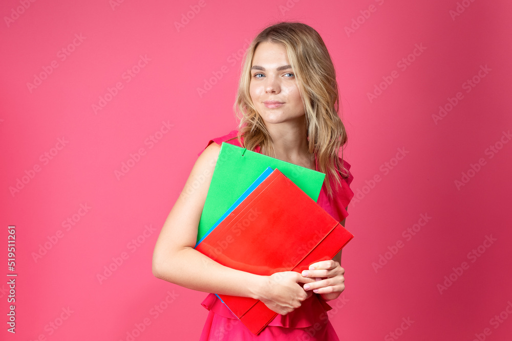 Young Winsome Smiling Caucasian Girl in Red Summer Dress With Colorful Folders Against Coral Background. Young Winsome Smiling Caucasian Girl in Red Summer Dress With Colorful Folders Against Coral Background.