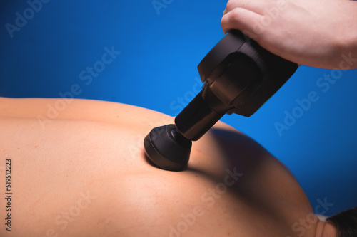 Physiotherapist treats the spine and back of a man with a massage percussion device. Physiotherapy, close-up, massage therapist
