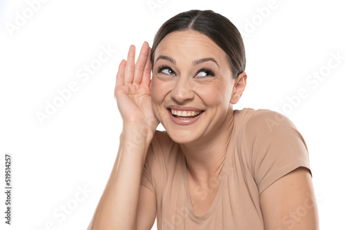 Smiling woman over isolated white background listening to something by putting hand on the ear