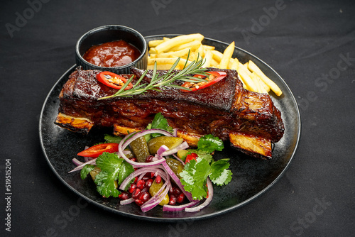 braised ribs in a plate with French fries on a black background macro photo
