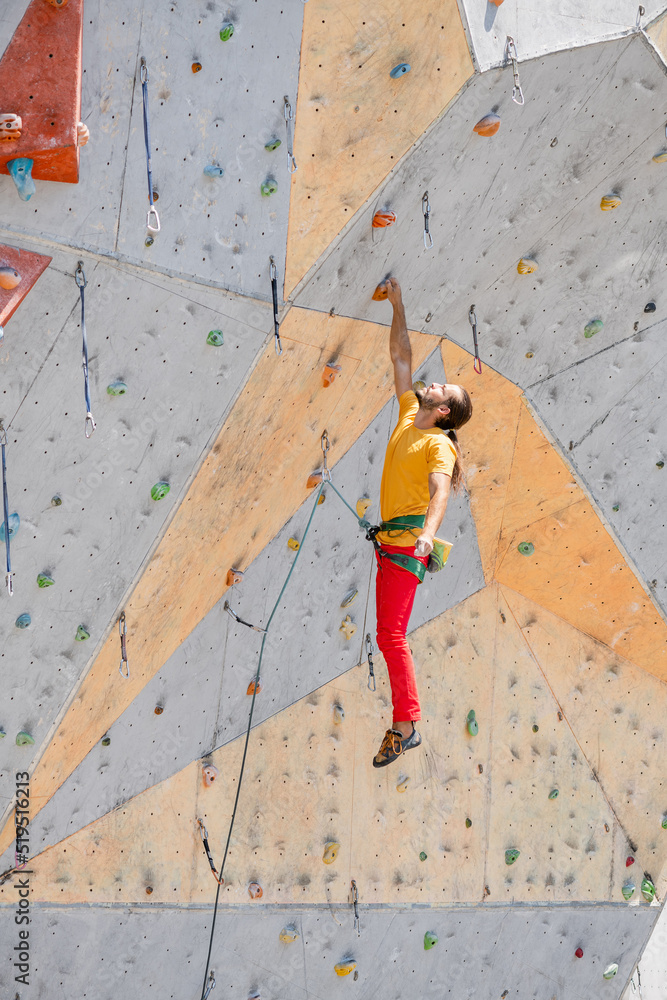 Sportsman climber hanging with one hand on an artificial climbing wall outdoors. Sportsman climber hanging with one hand on an artificial climbing wall outdoors.