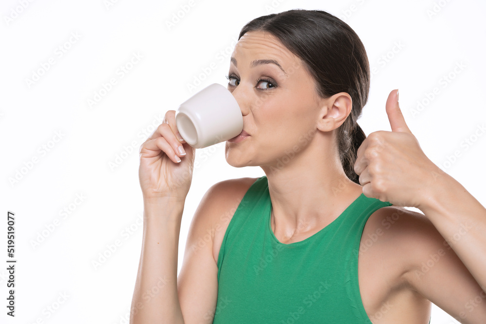 Happy young woman with cup of hot beverage showing thumb up on a white background Happy young woman with cup of hot beverage showing thumb up on a white background