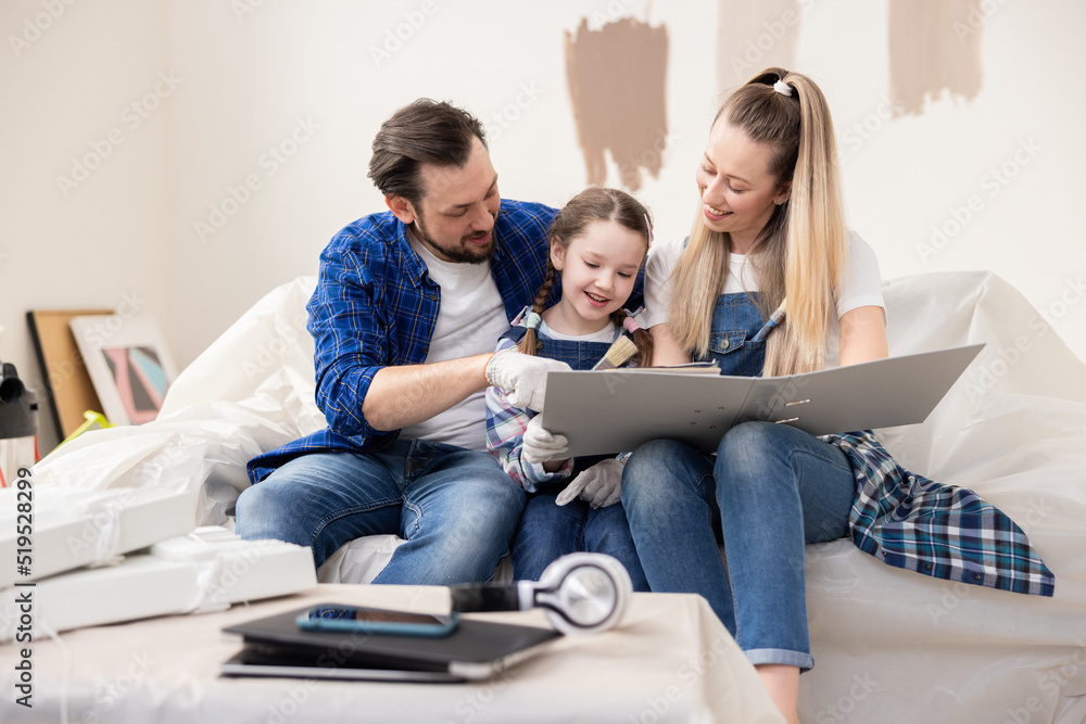 A middle-aged man, a child and a young, attractive woman are cheerfully discussing the future color of the walls. They are sitting in their new premises, in which they have started repairs. A middle-aged man, a child and a young, attractive woman are cheerfully discussing the future color of the walls. They are sitting in their new premises, in which they have started repairs.