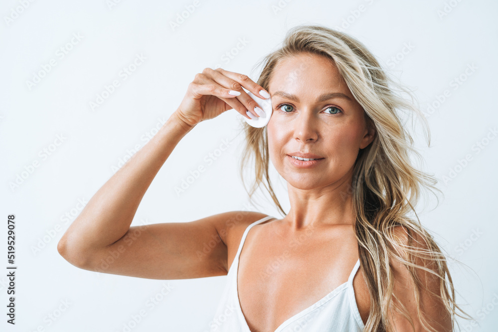 Beauty portrait of smiling blonde woman with clean fresh skin face with cotton pad in hand on white background isolated Beauty portrait of smiling blonde woman with clean fresh skin face with cotton pad in hand on white background isolated