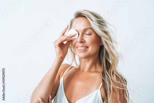 Beauty portrait of smiling blonde woman with clean fresh skin face with cotton pad in hand on white background isolated