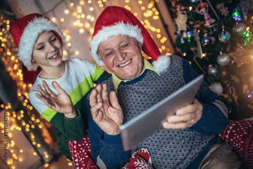Grandfather and grandson sitting on chair and looking at digital tablet during christmas. Senior man with a kid having a video call on digital tablet.
