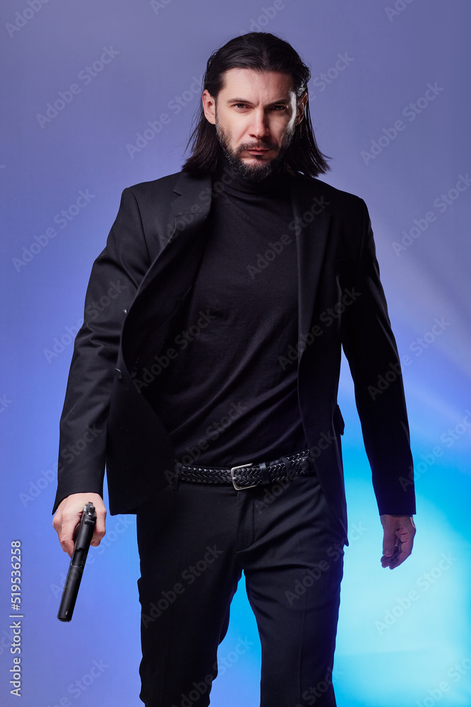 Fototapeta premium Studio portrait of bearded young man with gun, dressed as a spy or secret agent.