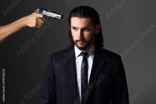 Studio portrait of bearded young man with gun, dressed as a spy or secret agent. © luengo_ua