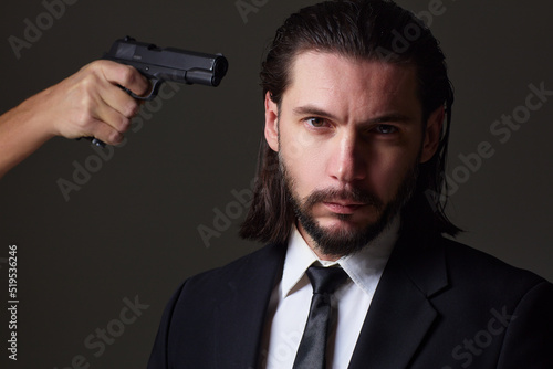 Studio portrait of bearded young man with gun, dressed as a spy or secret agent.