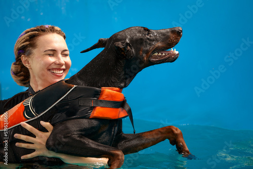 Schilderij op canvas Dog in life jacket swim in the swimming pool with coach