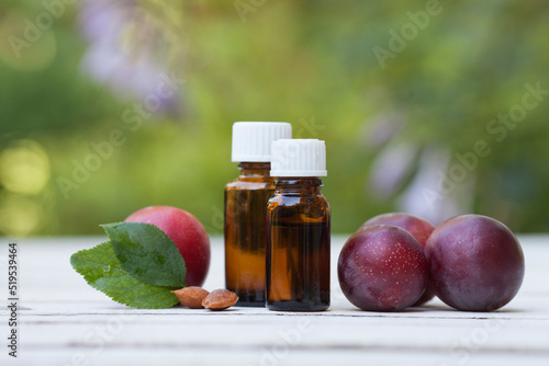 Plums bone's kernels essential oil with ripe plums on white wooden and greenery background