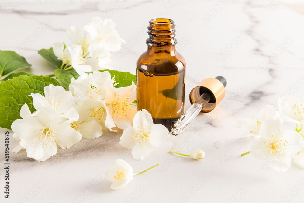 an open cosmetic bottle with organic jasmine oil and a filled pipette with a background of white jasmine flowers. natural cosmetics. an open cosmetic bottle with organic jasmine oil and a filled pipette with a background of white jasmine flowers. natural cosmetics.