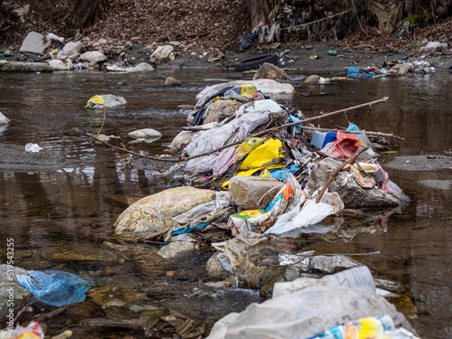 Tableau sur toile CLOSE UP: Pile of plastic waste jammed between the rocks in the middle of river