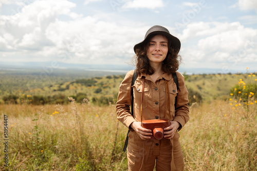 Happy female traveler in black hat posing and holding photo camera during safari, copy space
