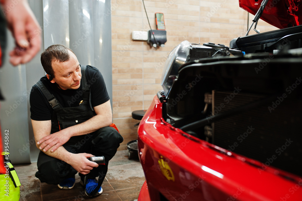 Car service worker put anti gravel film on a red car body at the detailing vehicle workshop. Car protection with special films. Car service worker put anti gravel film on a red car body at the detailing vehicle workshop. Car protection with special films.