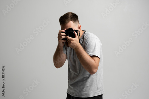 Handsome and confident man photographer with a large professional camera taking pictures photo shooting on the on the white background.