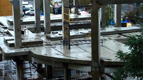 Construction site in the rain on the background of walking people, cars. The builders left the workplace due to bad weather. Concrete slabs and precast reinforced concrete piles are flooded with water