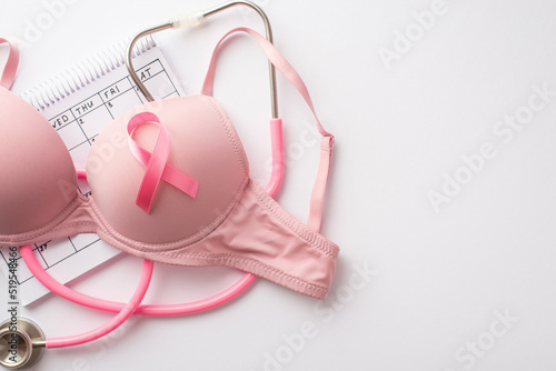 Breast cancer awareness concept. Top view photo of pink brassiere with pink ribbon stethoscope and calendar on isolated white background