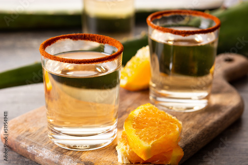 Mezcal Mexican drink with orange slices and worm salt on wooden table	