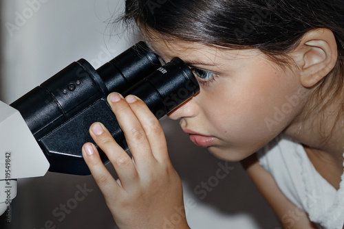 Girl schoolgirl curiously looks into a professional microscope exploring the world on a white background, day, back to school