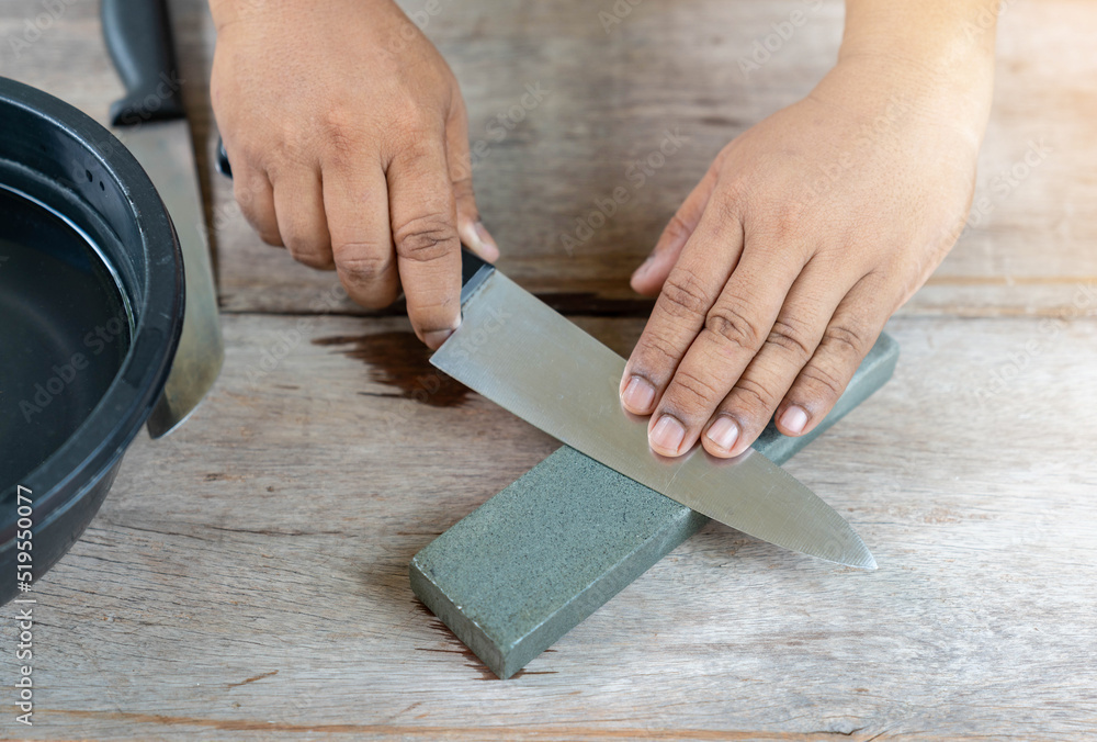 The man sharpen kitchen knife with whetstone on wooden table. The man sharpen kitchen knife with whetstone on wooden table.