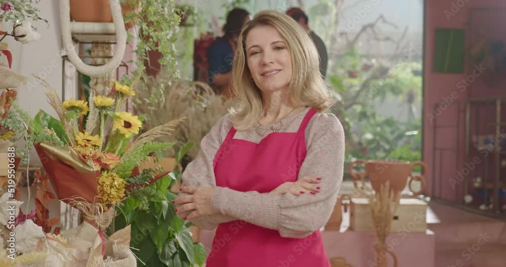 Businesswoman owner of small flower shop standing inside retail store smiling at camera while employees work in the background. Small business concept of female entrepreneur starting new business Businesswoman owner of small flower shop standing inside retail store smiling at camera while employees work in the background. Small business concept of female entrepreneur starting new business