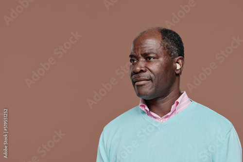 Portrait of senior deaf African man with hearing aid standing against brown background photo