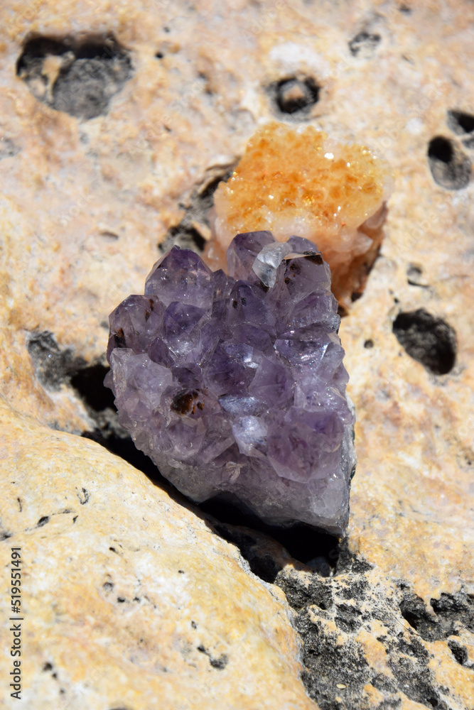 Beautiful purple crystals of amethyst and druse cetrinum on a yellow stone on the seashore. Bright purple amethyst druze in the shape of a heart against the background of the sea.