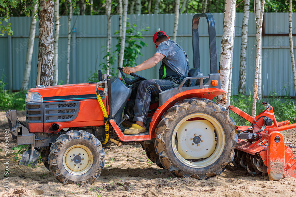Obraz premium A man on a mini-excavator levels a piece of land, loosens the soil.