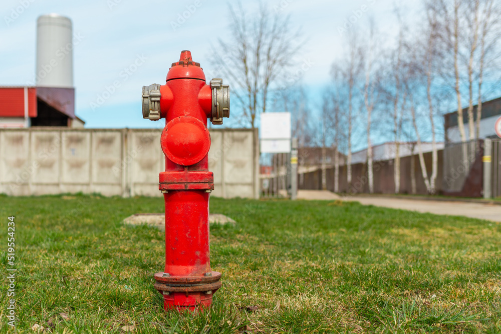 Single red fire hydrant on green lawn,blue sky.In a background factory.Autumn,spring,summer day. Single red fire hydrant on green lawn,blue sky.In a background factory.Autumn,spring,summer day.