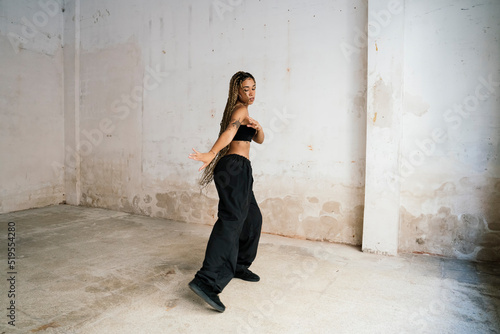 multiracial girl with long blonde braids dancing in a black tracksuit in an abandoned warehouse while smiling and enjoying her passion and exercise.