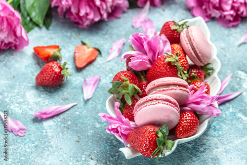 Pink peony rose flower and macaroni cookies and sweet strawberry on blue background. Small French cakes Macarons with fruit. top view