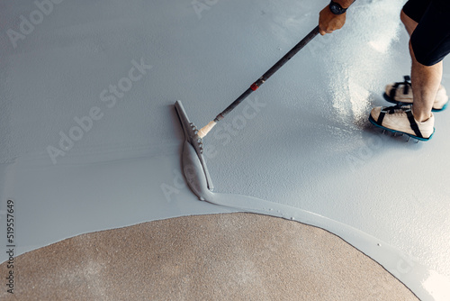 A construction worker apply grey epoxy resin in an industrial hall photo