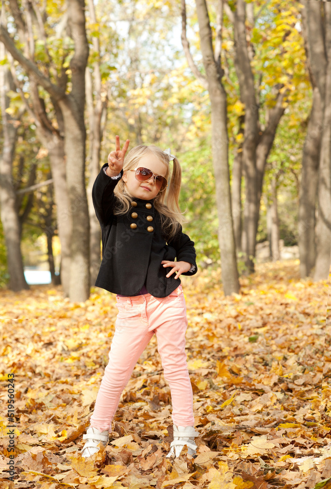 Little blonde girl posing showing victory in autumn park Little blonde girl posing showing victory in autumn park