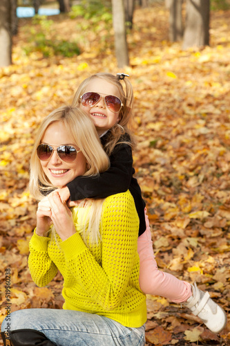 Young mother and little daughter portraits dressed in sunglasses in autumn park