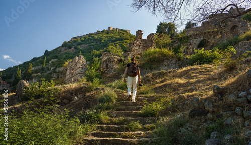 Tourist man with backpack exploring ruins of old city of Mystras, UNESCO world heritage archeological sight. photo