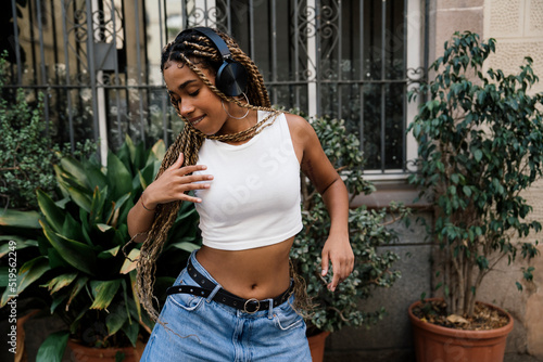 multiracial girl with long blonde braids dancing in a black tracksuit in the street while smiling and enjoying her passion and exercise.
