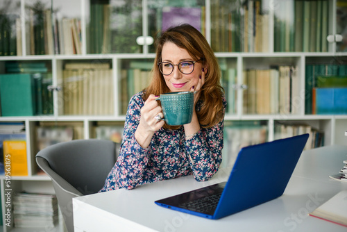 Businesswoman working on laptop in the library and holding a cup of coffee 