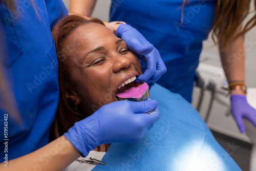 Close up of a female dentist s hands  placing an impression tray into one of her black female client s mouth  in order to take a sample denture at the dental clinic