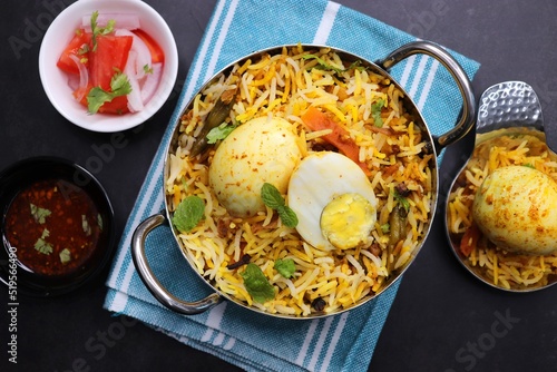 Egg dum Biryani or anda biryani Fragrant Basmati rice cooked with spicy masala gravy along with spices  veggies and boiled eggs. served with yogurt  salad and salan. Black background with copy space.