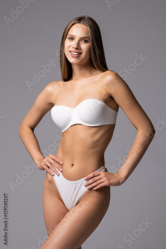 Attractive young woman in white lingerie posing against grey background and smiling © F8  \ Suport Ukraine