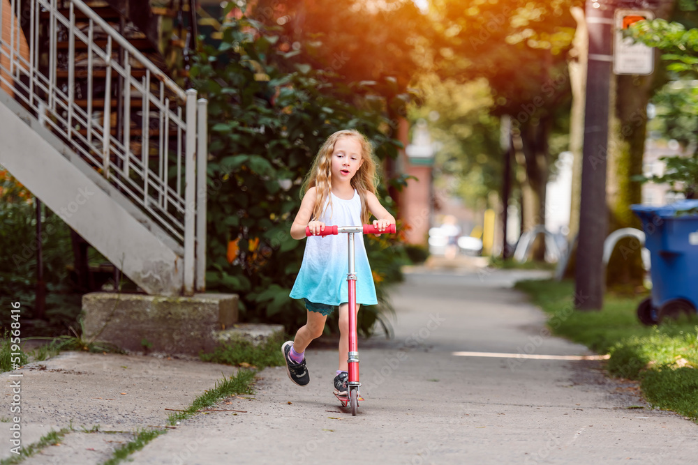 Portrait of active little girl riding scooter outdoors on summer day