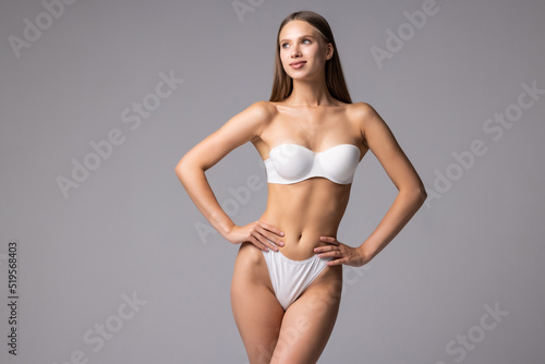 Attractive young woman in white lingerie posing against grey background and smiling
