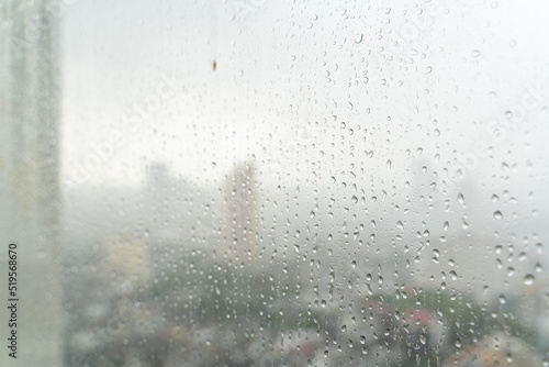Rain drop on glass window at day time in monsoon season with blurred city buildings background.