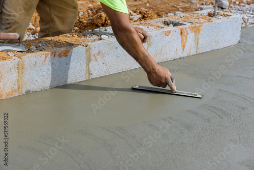 A masonry worker holds a steel trowel as he smoothes plastering concrete on a cement floor with a steel trowel