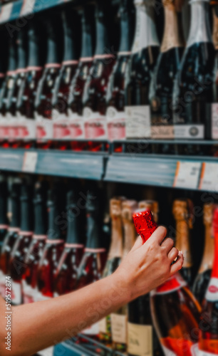 woman hand taking bottle of champagne wine from shelf at supermarket